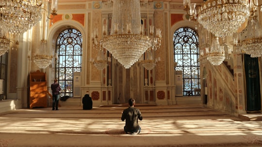 man in black jacket sitting on brown concrete floor in Ortaköy Mosque Turkey