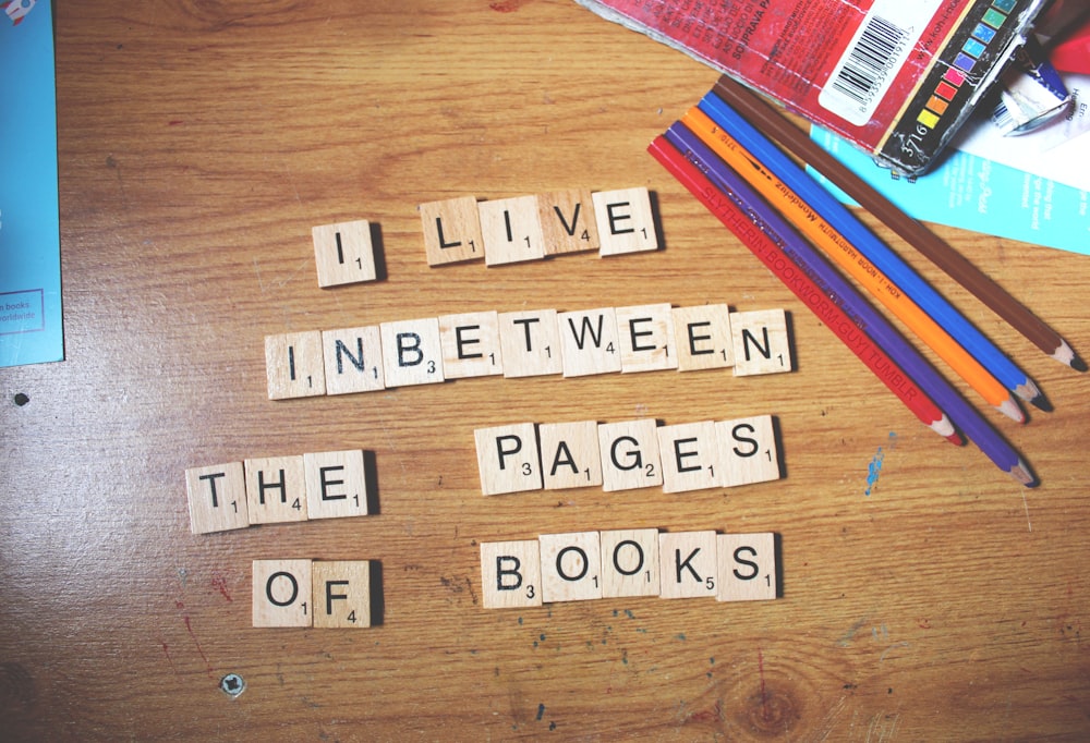 a wooden table topped with scrabble tiles and pencils