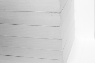 A close-up view of a neatly stacked pile of white paper sheets. The edges are perfectly aligned, creating a clean, precise visual appearance.