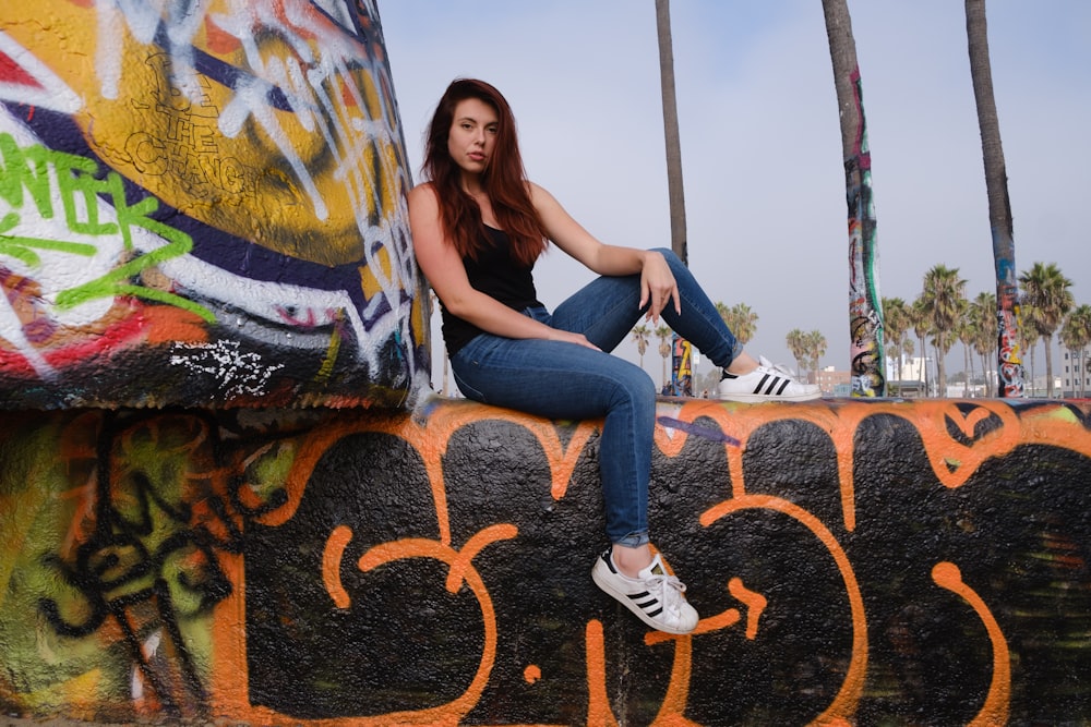 woman in black t-shirt and blue denim jeans sitting on brown concrete bench during daytime