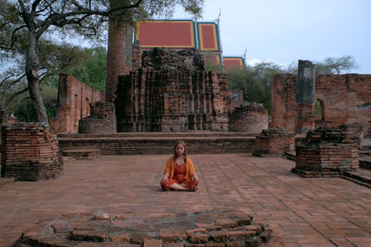 woman in red dress sitting on brown concrete bench during daytime in Ayutthaya Thailand