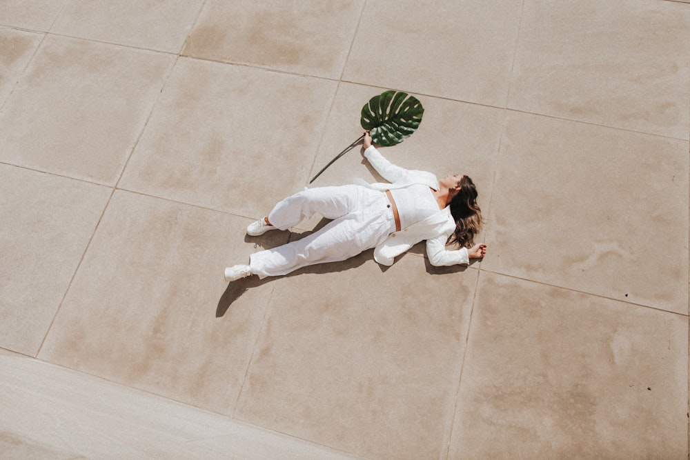 woman in white long sleeve shirt and white pants lying on green and white floor tiles