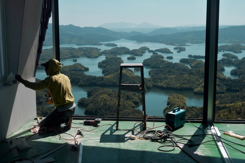 man in green shirt sitting on the edge of a building looking at the lake during