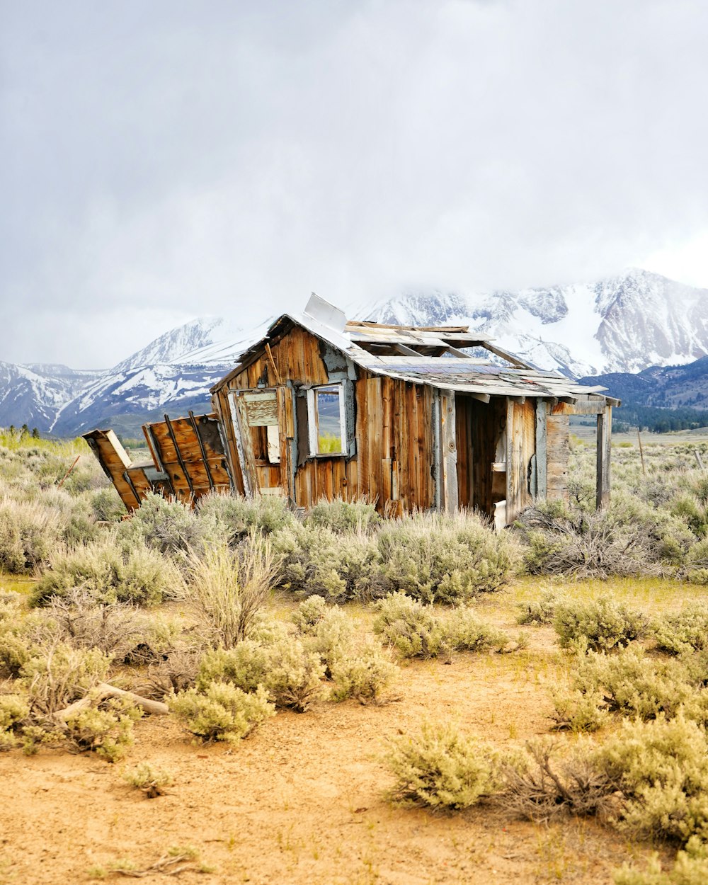 brown wooden house on green grass field near snow covered mountain during daytime