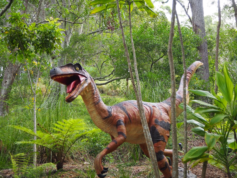 estátua marrom e preta do dinossauro na floresta durante o dia