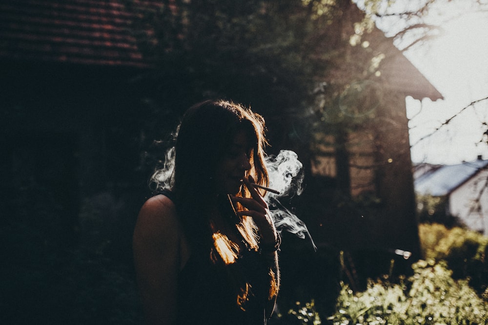 Une femme fumant une cigarette devant une maison