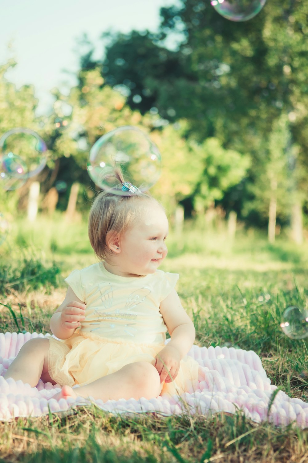baby in white dress playing with bubbles on green grass field during daytime