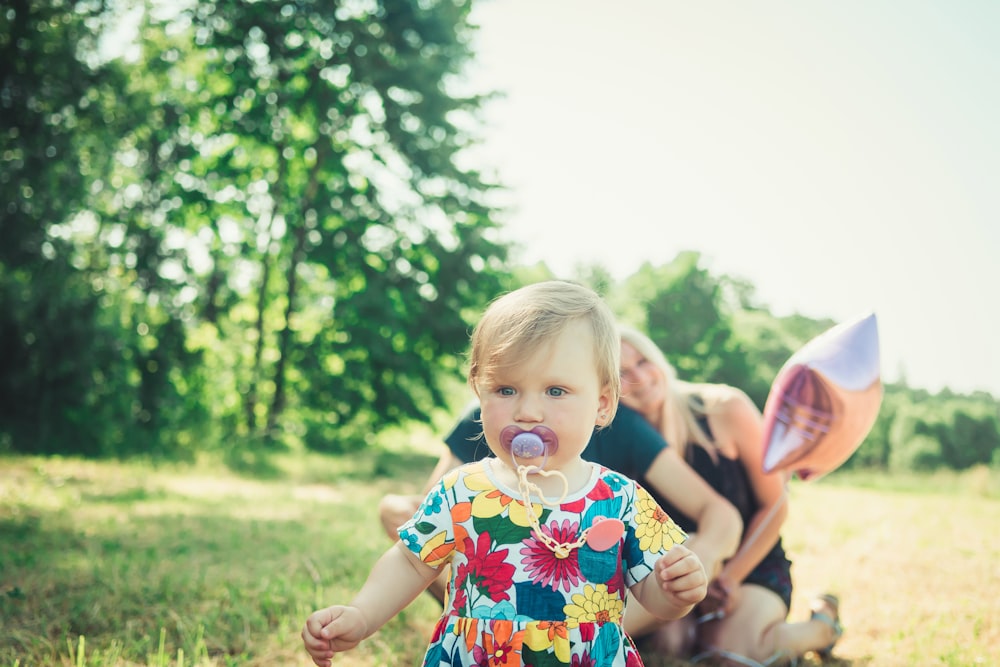 girl in blue white and red floral dress standing on green grass field during daytime