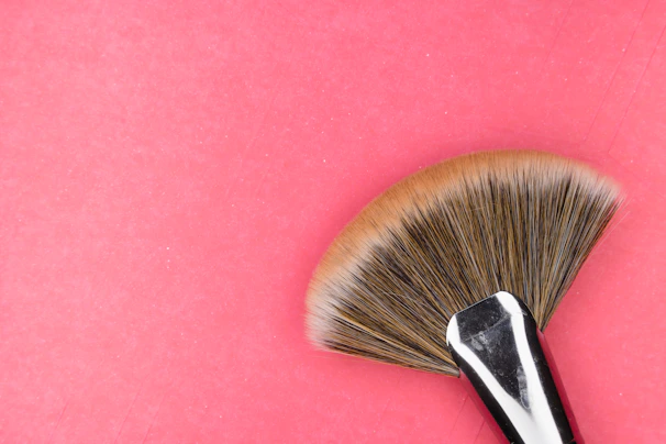 A hand holding a sleek, modern makeup brush with soft bristles against a pastel background.