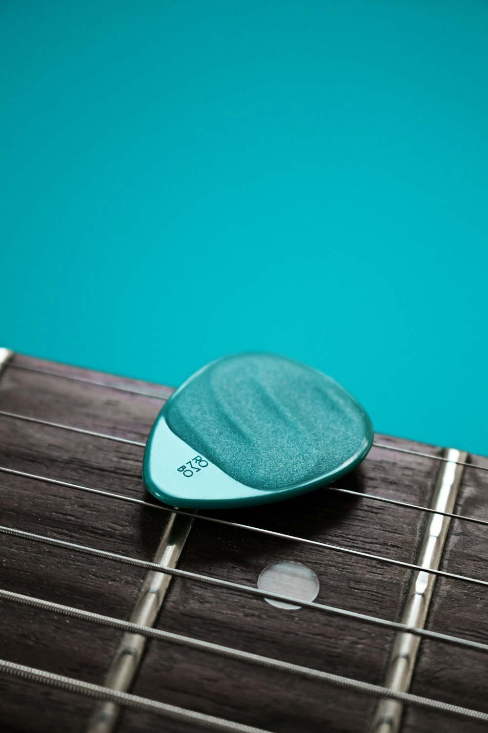 teal guitar pick on brown guitar