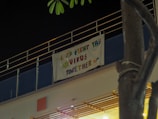 A banner hangs on the side of a building under dim lighting. The banner has the message 'Let's Fight The Virus Together' in colorful letters with a small illustration of a virus.