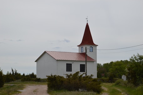 white and red church near green trees under white sky during daytime