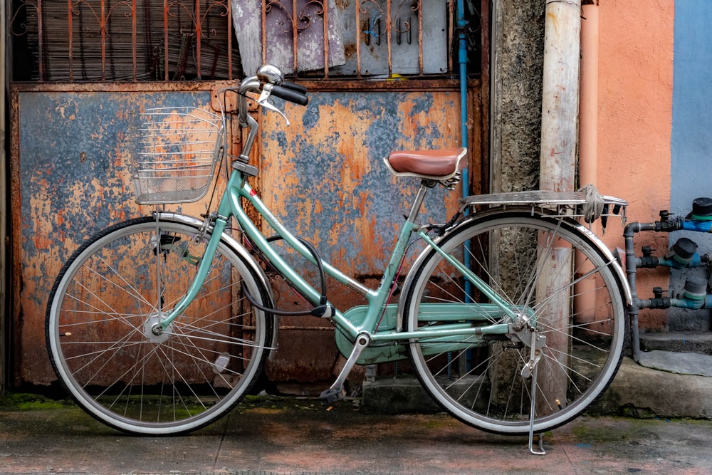 teal city bike parked beside brown concrete wall