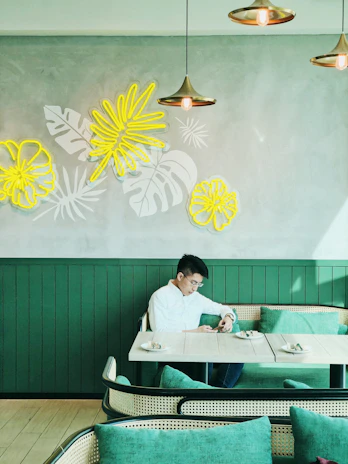 A relaxed man sitting in a modern café, wearing a crisp white shirt from the collection.