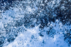 Dynamic splash of water droplets creating a chaotic pattern against a dark background, with varying sizes and transparency of the water particles.