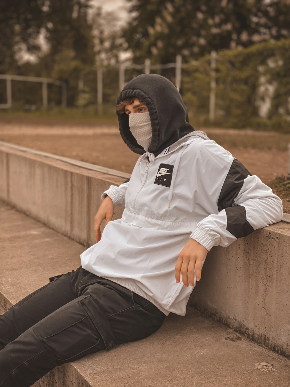 man in white and black adidas hoodie and black pants sitting on concrete bench during daytime