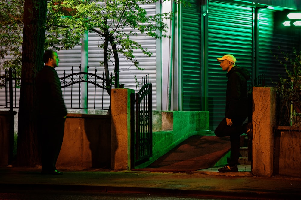 man in black jacket and yellow hat standing near green house during daytime