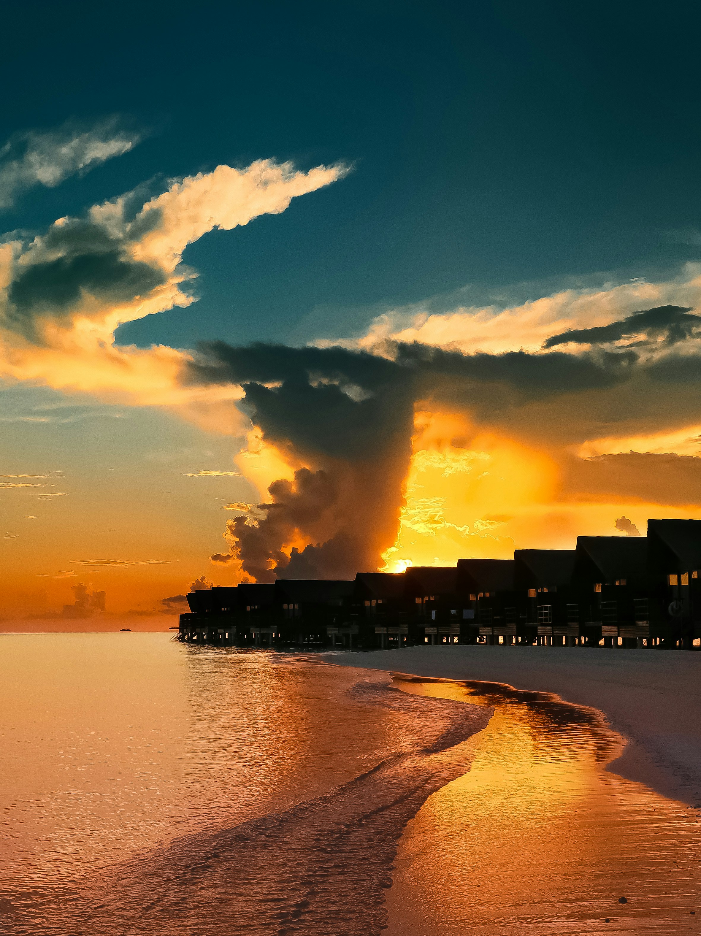 Maldives overwater bungalows at golden hour, dark teal ocean, dramatic clouds, deep shadows on wooden walkways