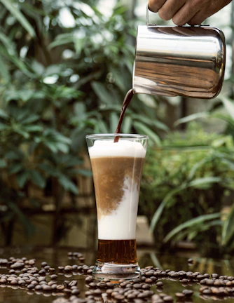Friendly barista pouring a creamy smoothie into a glass with a beach scene visible through the window.
