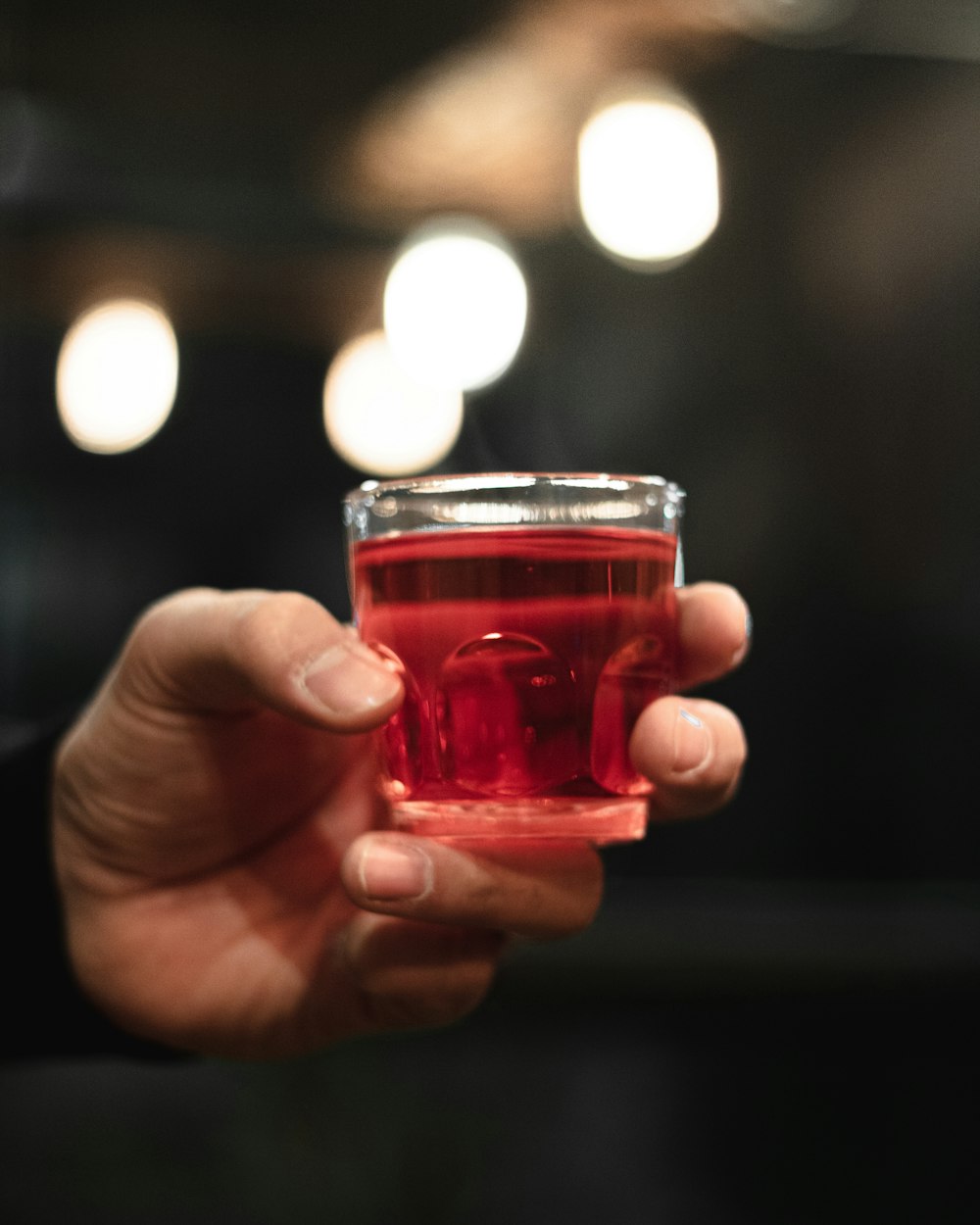 person holding clear glass cup with red liquid