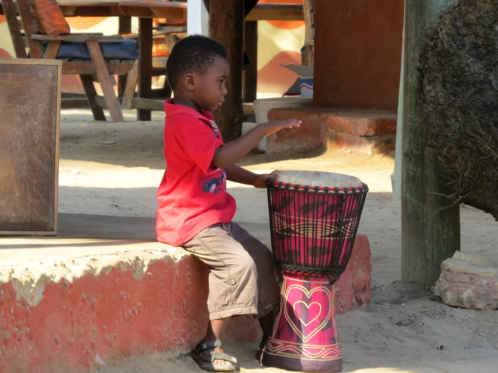빨간 티셔츠를 입은 소년이 드럼을 연주하고 있다