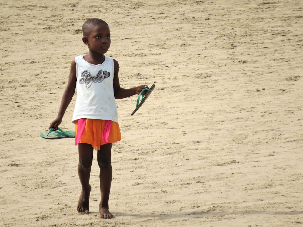 girl in white tank top and red shorts standing on white sand during daytime