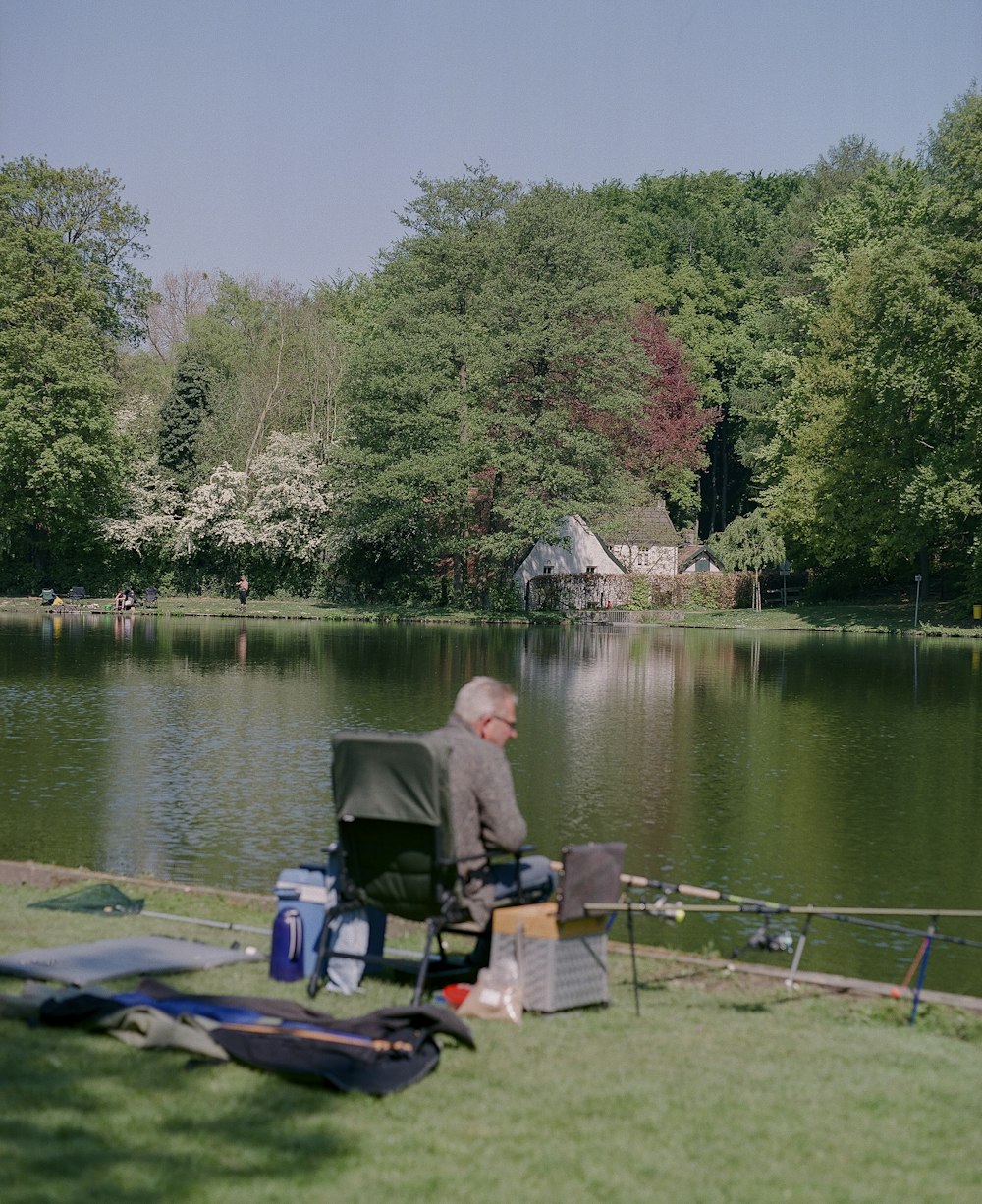 man in gray jacket sitting on green chair near lake during daytime