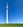 A large wind turbine stands prominently against a clear blue sky, situated on a lush green field. Its blades are positioned to capture wind energy efficiently.