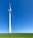 A large wind turbine stands prominently against a clear blue sky, situated on a lush green field. Its blades are positioned to capture wind energy efficiently.