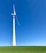 A large wind turbine stands prominently against a clear blue sky, situated on a lush green field. Its blades are positioned to capture wind energy efficiently.
