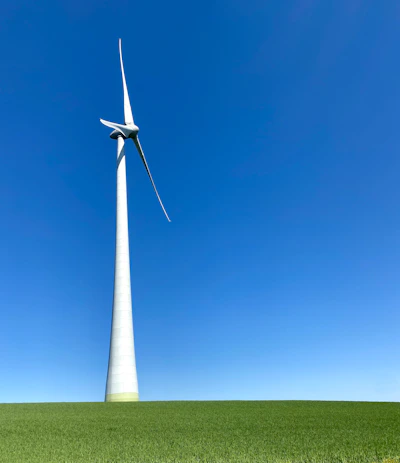 A compact wind turbine standing tall on a green farm field under a clear blue sky.