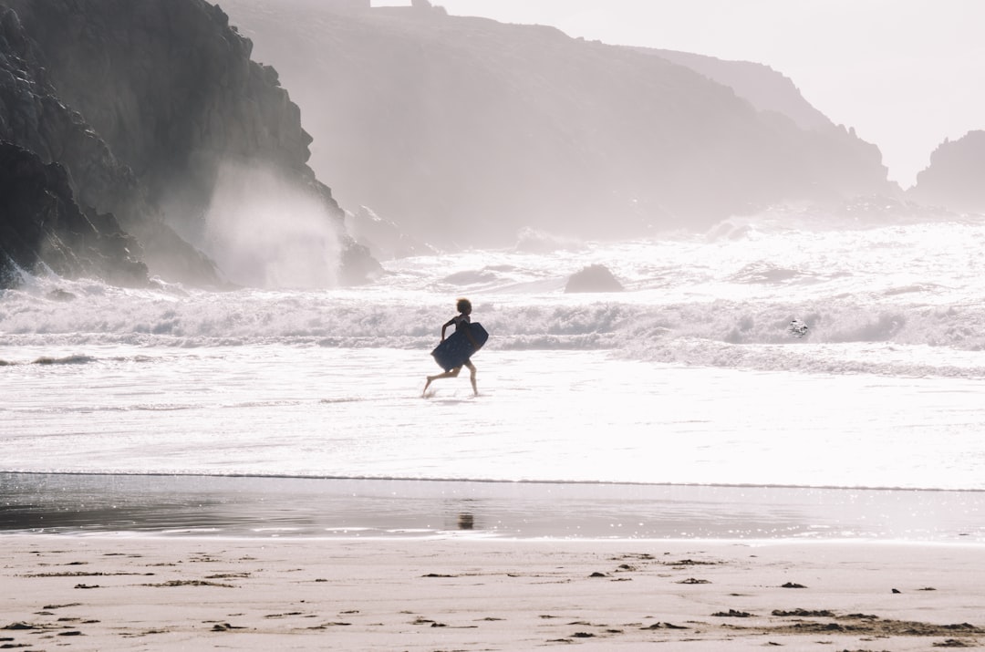 woman in black jacket and white pants walking on seashore during daytime