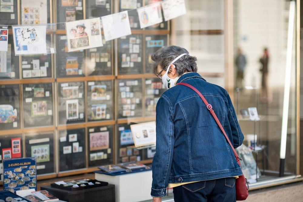 man in blue denim jacket standing near brown wooden shelf