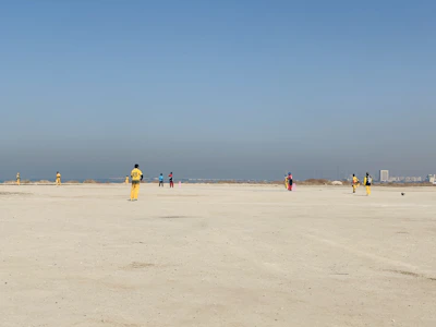 Children in colorful sports gear practicing cricket on a bright green field under a clear blue sky.