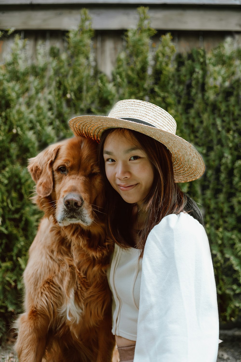 woman in white shirt and brown hat holding brown long coated dog