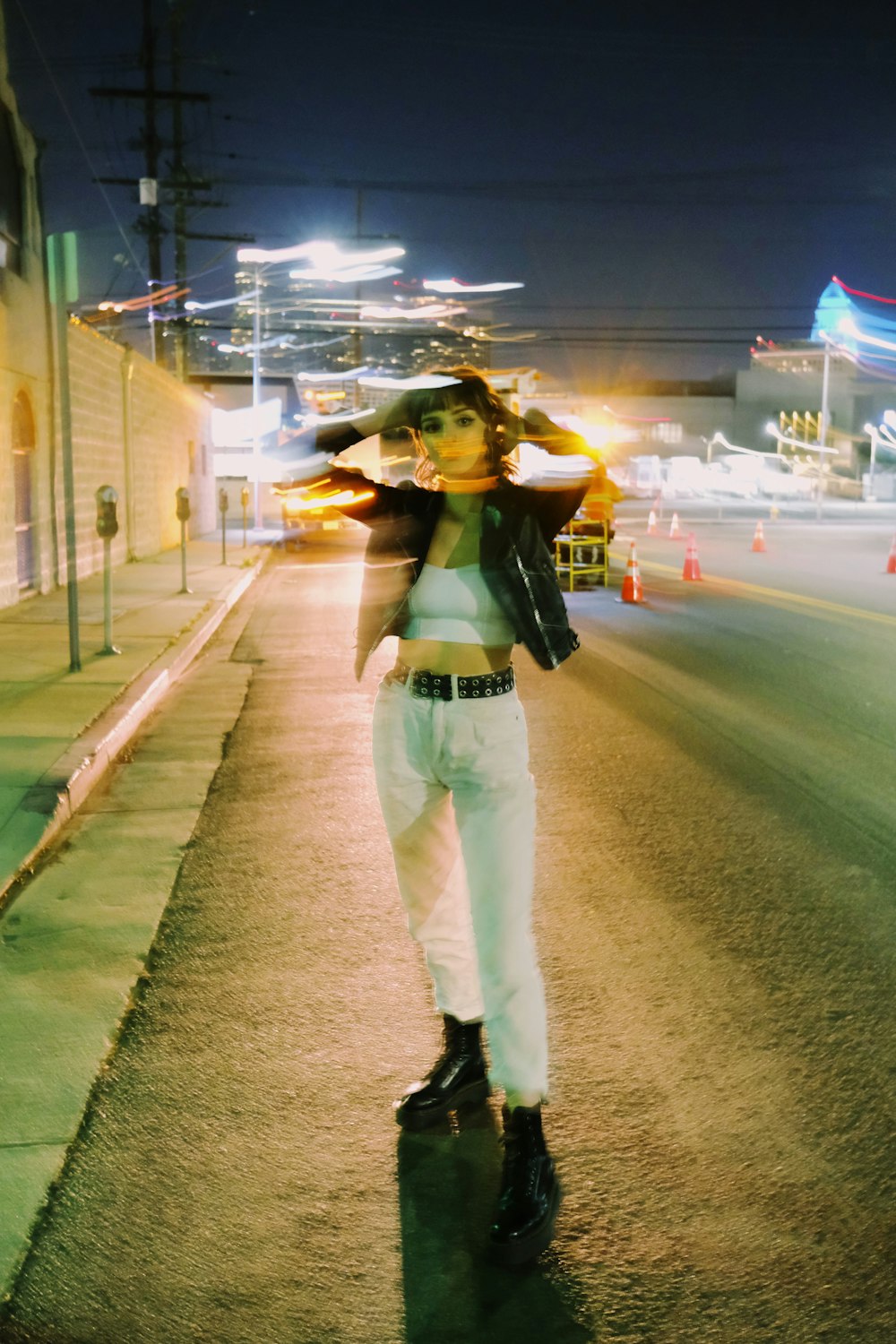woman in green shirt and white pants standing on road during night time