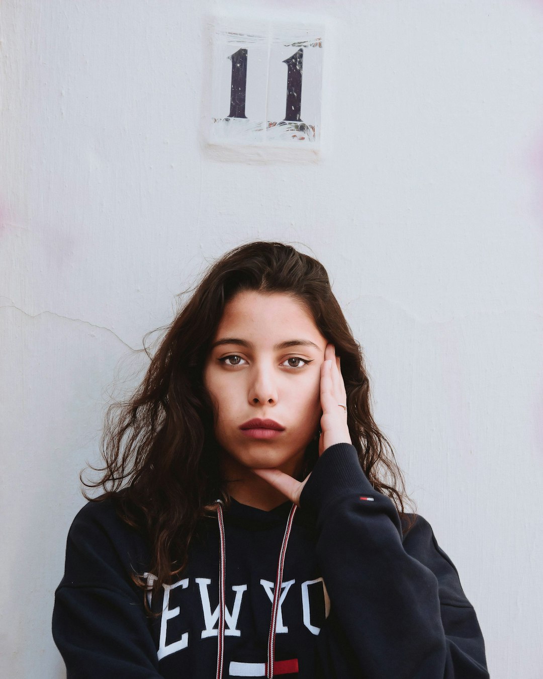 woman in black hoodie leaning on white wall