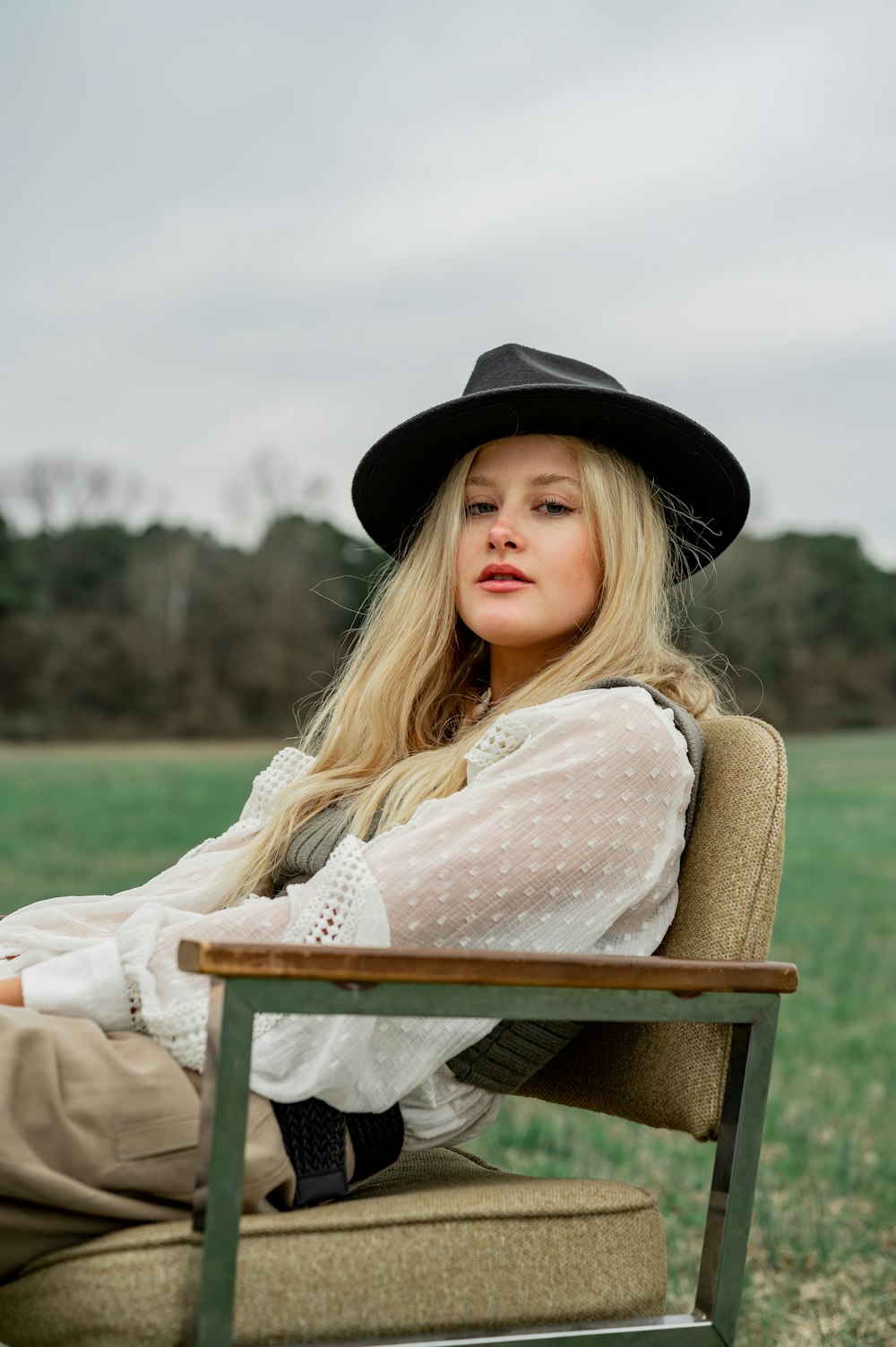 woman in white long sleeve shirt and black hat sitting on brown wooden chair