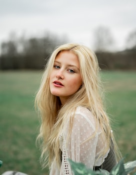 woman in white lace shirt standing on green grass field during daytime