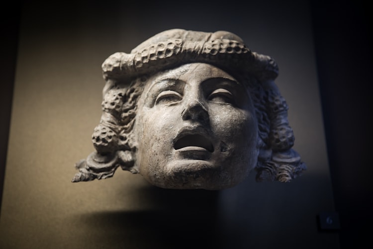 An ancient stone head with headdress, shot from below in a darkened room, the mouth is open