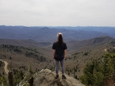 woman in black jacket standing on rock formation during daytime wilderness zoom background