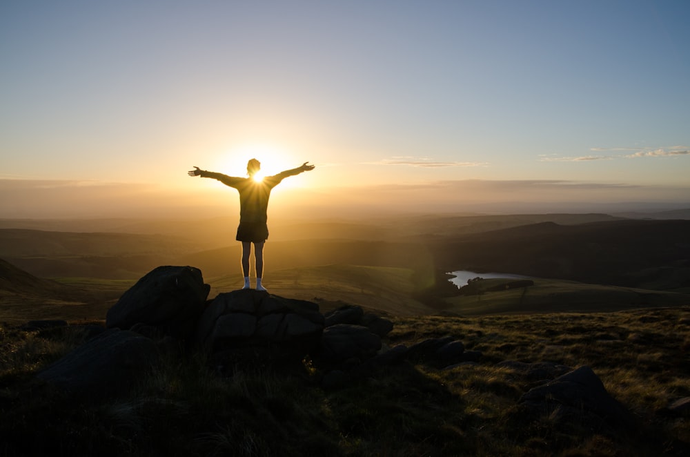 silhouette of person standing on rock during sunset