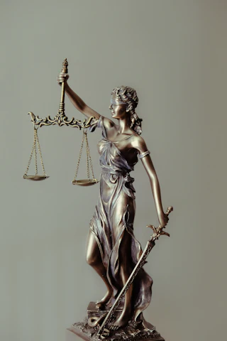 A bronze Lady Justice statue holds balanced scales and a downward sword while blindfolded