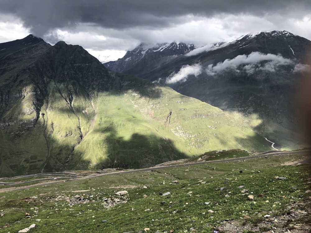 green grass field near mountain under white clouds during daytime