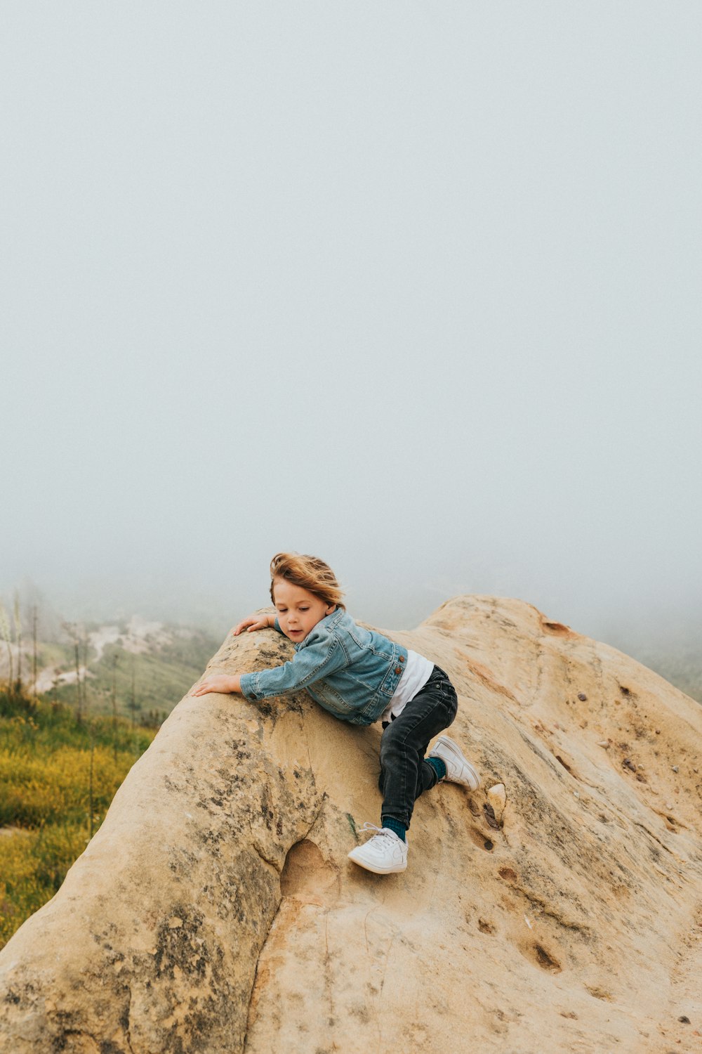 woman in blue denim jacket and black pants sitting on brown rock during daytime