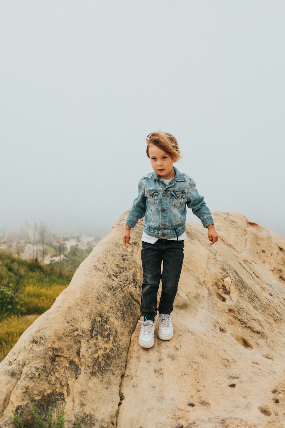 boy in blue denim jacket standing on brown rock during daytime