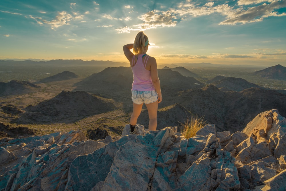 woman in pink shirt and white shorts standing on rocky mountain during daytime