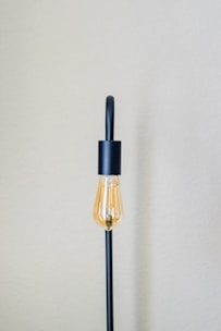 A minimalist Scandinavian lamp with a warm glowing bulb and a simple white shade on a cozy linen-covered side table.