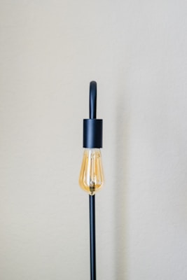 A minimalist Scandinavian lamp with a warm glowing bulb and a simple white shade on a cozy linen-covered side table.