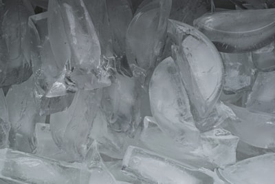 A collection of irregularly shaped ice cubes piled together, creating a textured and translucent appearance with various angles reflecting light.